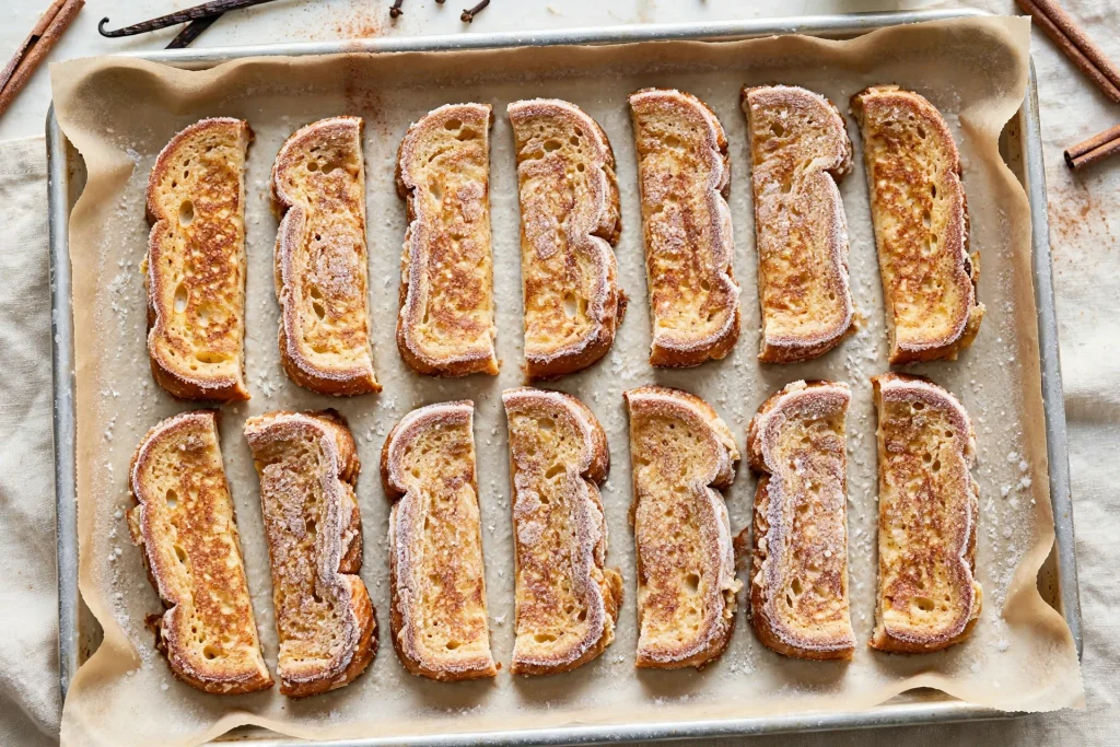French toast sticks arranged on a parchment-lined baking sheet before freezing.
