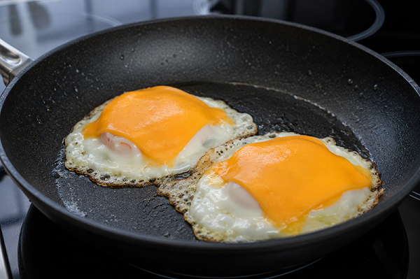 Fried eggs topped with melting cheddar cheese slices in a skillet.